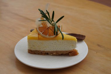 honey slice, dry orange slice, green leaf, wooden spoon, on yuzu cheese pie on white ceramic plate on wooden table background, food, dessert, health, copy space                                        