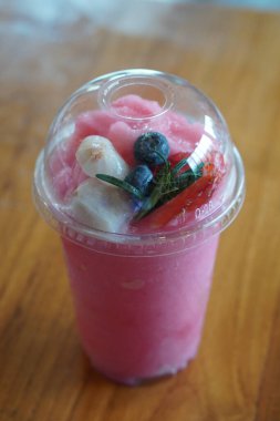 Tahta zeminde plastik bir bardakta lychees ve yaban mersinli taze çilekli smoothie. yiyecek, meyve, tatlı, buz, soğuk, kopyalama alanı                                   