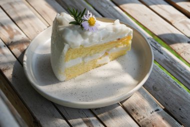 Yakın plan Hindistan cevizli pasta sarı polen ve menekşe çiçekleri ile süslenmiş ve yeşil yapraklar bambu masa arka planında seramik bir tabakta, yemek, tatlı, kopyalama alanı                                                              