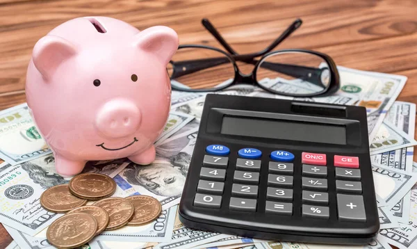 Hesap makineli, gözlüklü, banknotlu ve bozuk paralı bir domuz kumbarası. İş konsepti. 