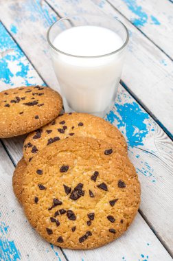 Eski mavi ahşap masada bir bardak süt ve çikolatalı kurabiye..