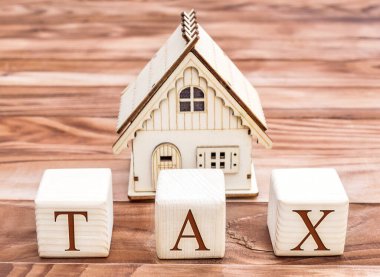 Tahta küplerde kelime vergisi ve ahşap arka planda ev modeli var. Emlak vergisi kavramı.