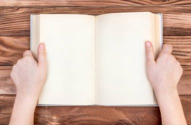 Çocuğun elleri ahşap masanın üzerinde boş bir kitap tutuyor. Üst görünüm.