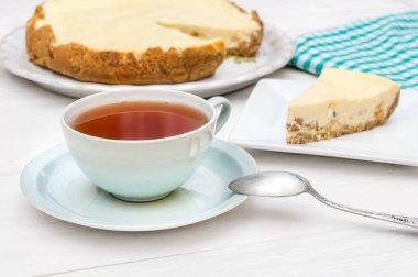 Masanın üzerinde bir parça peynirli kek ile bir fincan çay..