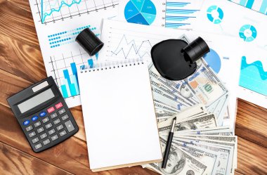 Finansal belgelerle dolu boş bir not defteri, işyerine dökülen ham petrol, para ve hesap makinesi. Üst görünüm.