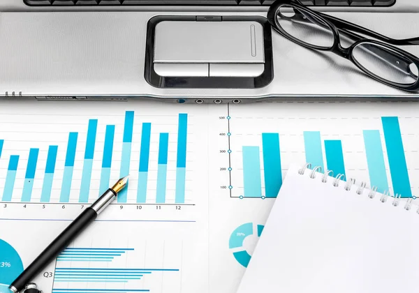 stock image Financial graphs with laptop, eyeglasses, pen and notepad on the workplace.