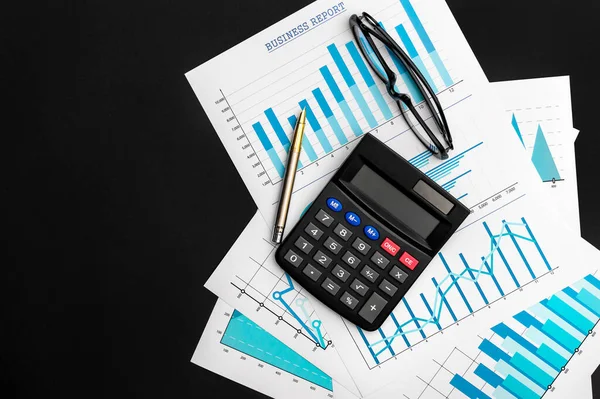 Financial graphs with calculator, eyeglasses and pen on black background. Top view. Copy space for text.