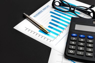 Finansal grafikler, hesap makinesi, gözlükler ve siyah arka planda kalem. İş konsepti.