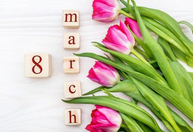 Tahta küplerin üzerinde 8 Mart tarihi ve ahşap arka planda laleler var. Tatil geçmişi. Üst görünüm.