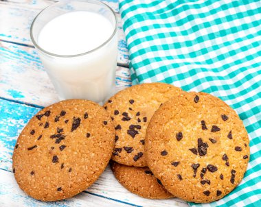Çikolata parçalı kurabiyeler, bir bardak süt ve mutfak havlusu eski mavi ahşap masada..