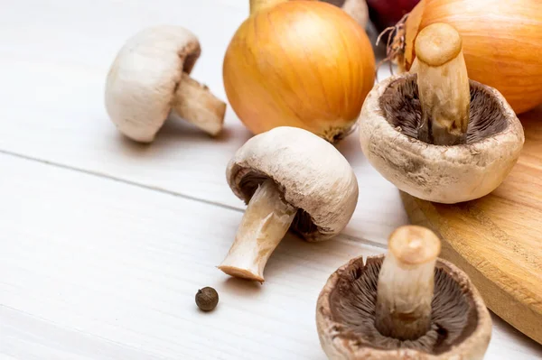 stock image Mushrooms and onions with cutting board on the white wooden table.