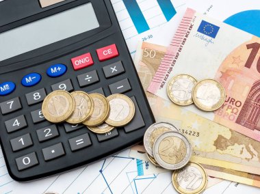İş grafiklerinde hesap makinesi olan Euro banknotları ve madeni paralar. Üst görünüm.
