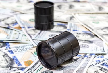 Dolar banknotlarının arka planında iki varil ham petrol var..