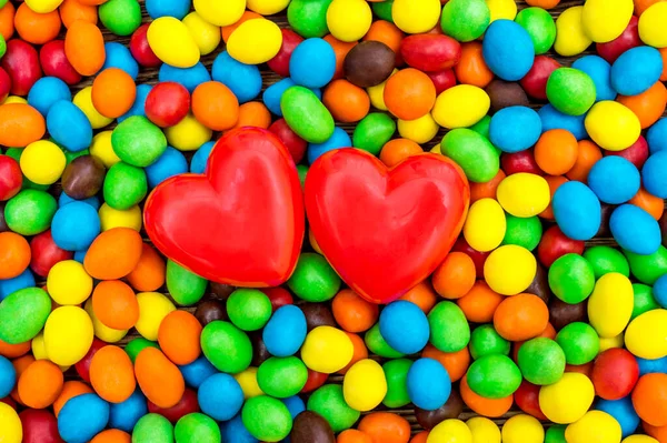 两颗红心在甜甜的圆形糖果的背景上 顶部视图 图库照片