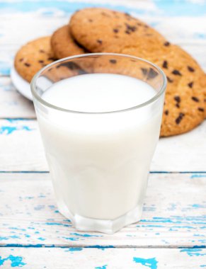 Eski mavi ahşap masada çikolatalı kurabiye ve bir bardak süt..