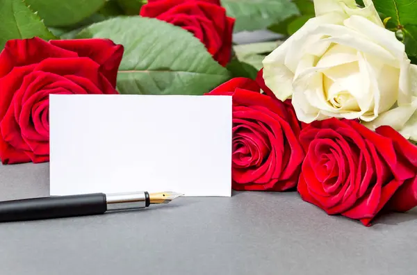 White and red roses with blank white card and pen on a  grey background.