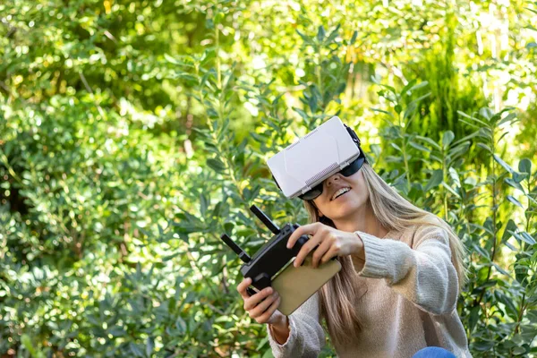 Happy, smiling and enthusiastic young woman controlling a drone with fpv technology for aerial video recording in nature