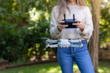 Şehir parkında küçük bir dronu kontrol eden ve uçuran tanınmayan genç bir kadının ön görüntüsü.