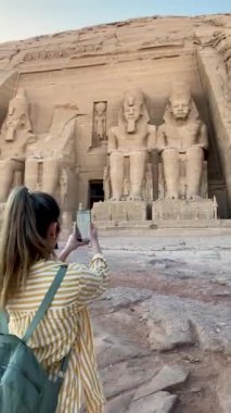 Vertical view of backwards tourist woman taking photos for social media to Abu simbel temple in Egypt, Africa