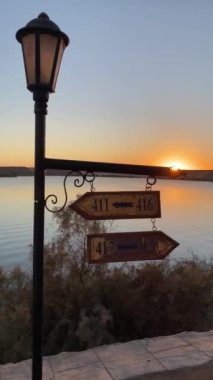 Vertical view of arrow shape posting sign in a streetlight moving and in movement in front of a flat lake at sunset time ine gypt