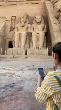Vertical view of backwards tourist woman taking photos for social media to Abu simbel temple in Egypt, Africa