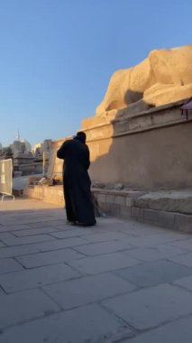 Vertical view of unrecognizable arab muslim man from the back while sweeping the street floor outdoors under blue sky