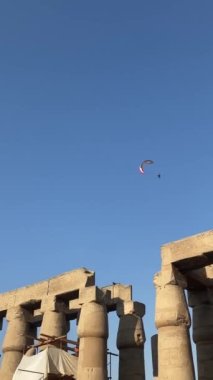 Mavi gökyüzünün ve etrafındaki kuşların altındaki bir Mısır tapınağının üzerinde uçan yamaç paraşütünün dikey görüntüsü