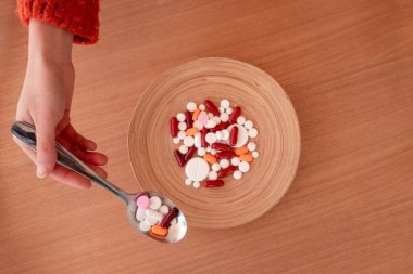 İsimsiz bir kadın eli, tahta masaya koyduğu kaşıkla renkli haplar alıyor.