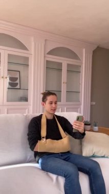 Kırık elli sıradan giysili genç adam doktorla video konferansı yoluyla konuşmak için cep telefonu kullanıyor.