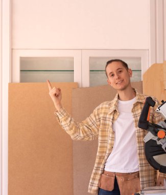 Damalı gömlekli genç işçi marangozluk makinesinin yanında dikiliyor ve...