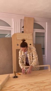 Yüzü olmayan erkek marangoz, atölyede mobilya montajı yaparken tornavidayla birlikte çekicin yanındaki tahta masaya vidalanıyor.