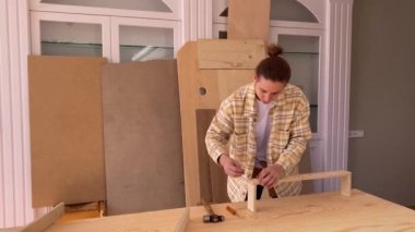 Yüzü olmayan erkek marangoz, atölyede mobilya montajı yaparken tornavidayla birlikte çekicin yanındaki tahta masaya vidalanıyor.