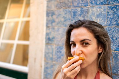 Yakın plan, Genç bir kadının geleneksel Portekiz Pastel de Nata 'nın tadını çıkartırken Gün Işığında Yatay Olarak Mavi Döşeme Duvarı' na Karşı,