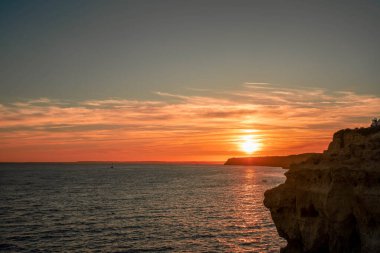 Okyanusa bakan kayalık bir uçurumun sakin günbatımı batan güneşin ılık parıltısını derin turuncu gökyüzüne karşı yakalıyor.