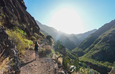Geniş açı görüntüsü, yüksek tepe ve vadilerin ihtişamı arasında engebeli bir dağ yolunu takip eden yalnız bir yürüyüşçüyü yakalar. Yürüyüşçülerin kıyafetleri yolculuk için hazır olduklarını gösteriyor. Sabahın erken saatlerinde güneş ruhani bir parıltı saçar.