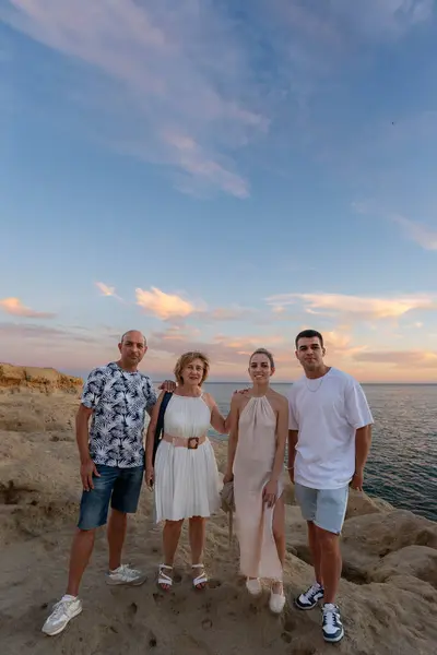 Family Bonding at Sunset: Vertical Shot of a Family of Four, Two Adults and Two teenagers, Standing on a Rocky Cliff Overlooking the Ocean at Sunset