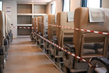 Modern bir tren vagonunun yatay çerçevesi. Resim, kırmızı ve beyaz bariyer bantlarıyla kapatılmış birçok boş bej koltuğu gösteriyor..