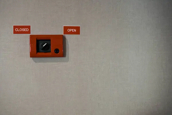 Close-up view of a red switch box mounted on a textured grey wall. The switch with labels OPEN and CLOSED. Captured in neutral light, the image represents the concept of access control.