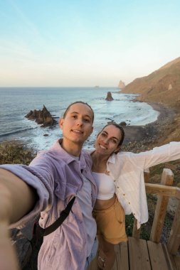 Bir çift, Benijo sahilinde, Tenerife, İspanya 'da geniş bir okyanus manzarasına bakan sakin bir günbatımı anını selfie ile yakalıyor..