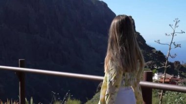 Bir kadın Tenerife, Masca Vadisi 'nde bir balkonda duruyor. Etrafındaki dağların nefes kesici manzarasını huzur içinde seyrediyor..