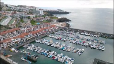 Parlak okyanusun yanındaki sayısız tekneyle dolu büyüleyici bir marinanın insansız hava aracı görüntüsünü alın..
