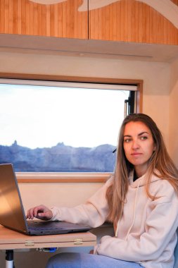 A digital nomad sitting at a desk inside a van, using a laptop computer to work remotely. clipart