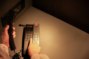 Bir insan eli, bir telefon ahizesini kavrar ve bir masa telefonundan bir numarayı çevirir. Geceleri hafif aydınlık bir ofis ortamında bir iletişim anını vurgular..