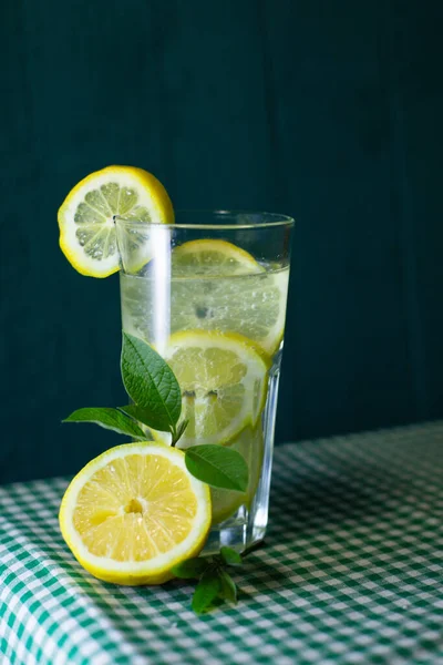 新鮮なレモンと緑の葉で飾られたレモネードの透明なガラスは美しい背景に — ストック写真