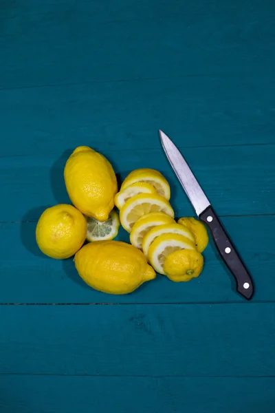 fresh lemons cut into slices on a blue background with a wooden texture with a knife
