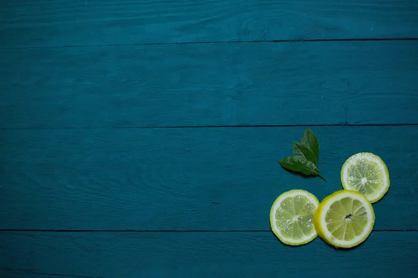 木の質感の青の背景に緑の葉のフレッシュなレモンのスライス — ストック写真