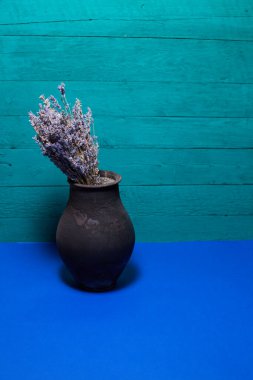 Mavi arka planda lavanta çiçekli siyah sürahi.