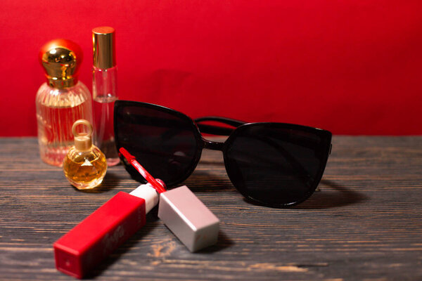 women's accessories on a red and black background, lipstick, glasses, perfume