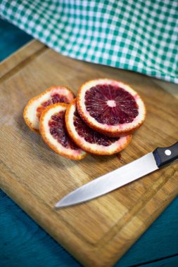 Taze Sicilya portakalı dilimlere ayrılmış mutfak bıçağı ve güzel ahşap bir tahta üzerinde damalı masa örtüsüyle mavi arka planda.