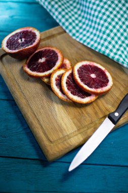 Taze Sicilya portakalı dilimlere ayrılmış mutfak bıçağı ve güzel ahşap bir tahta üzerinde damalı masa örtüsüyle mavi arka planda.